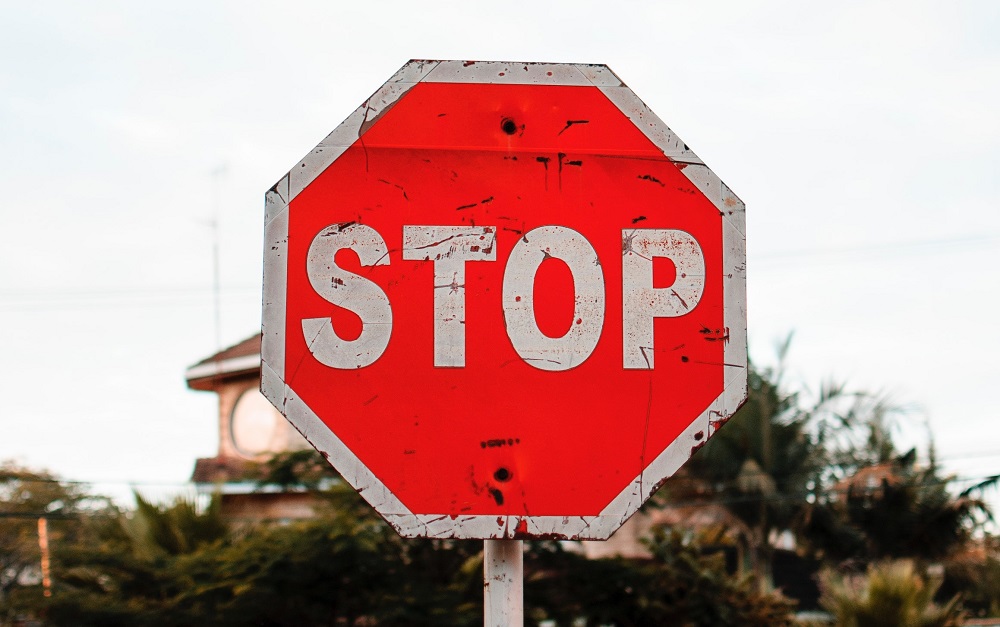 Closeup of a bright red, beat up stop sign with the sky and palm trees in the back, meant to represent the movement to stop mental illness stigma.