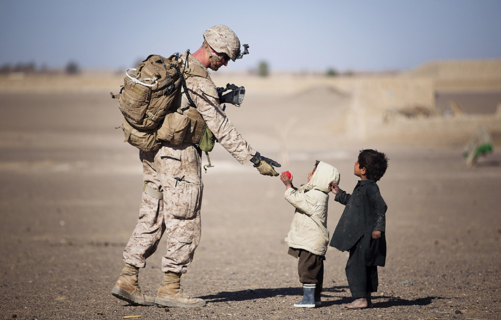 A soldier overseas in the desert, interacting warmly with two local toddlers. The photo is meant to represent the potential effects of moral injury.
