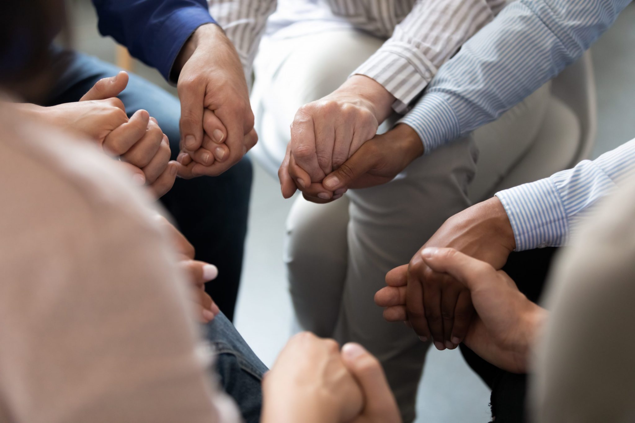 Closeup of people holding each other's hands at an Alcoholics Anonymous meeting as when the Serenity Prayer is recited.