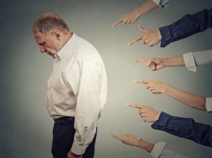 An older man hangs his head low as six arms point fingers at his back, meant to signify the stigma and shame that can be associated with substance abuse and the elderly.