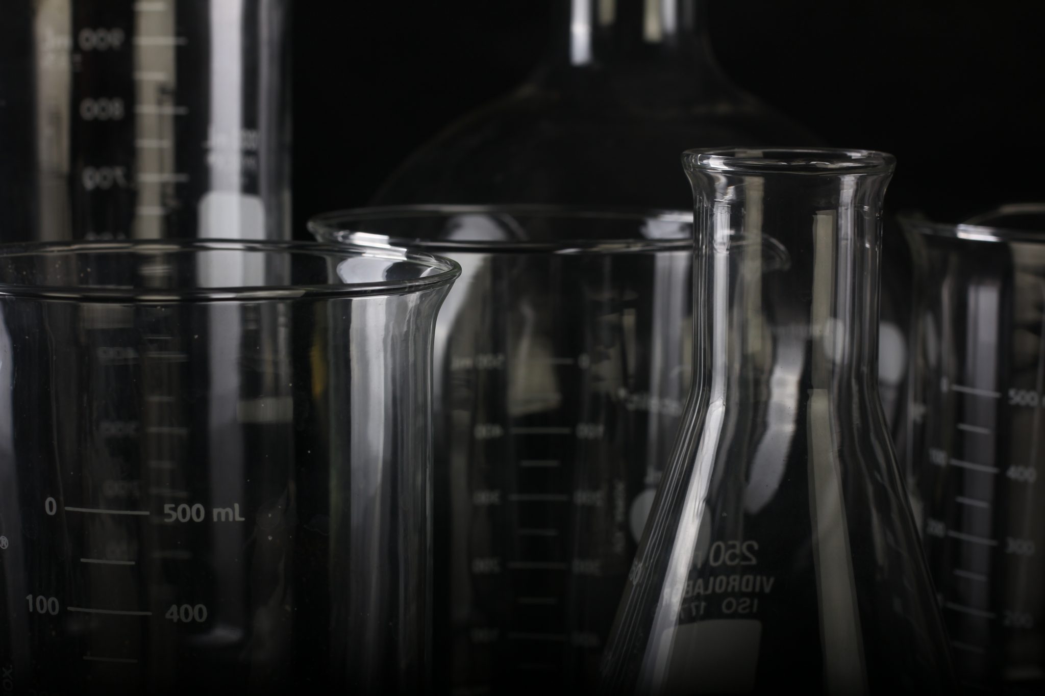 Scientific glass flasks and beakers of various sized against a black background, symbolizing the opioid fentanyl overdose crisis.
