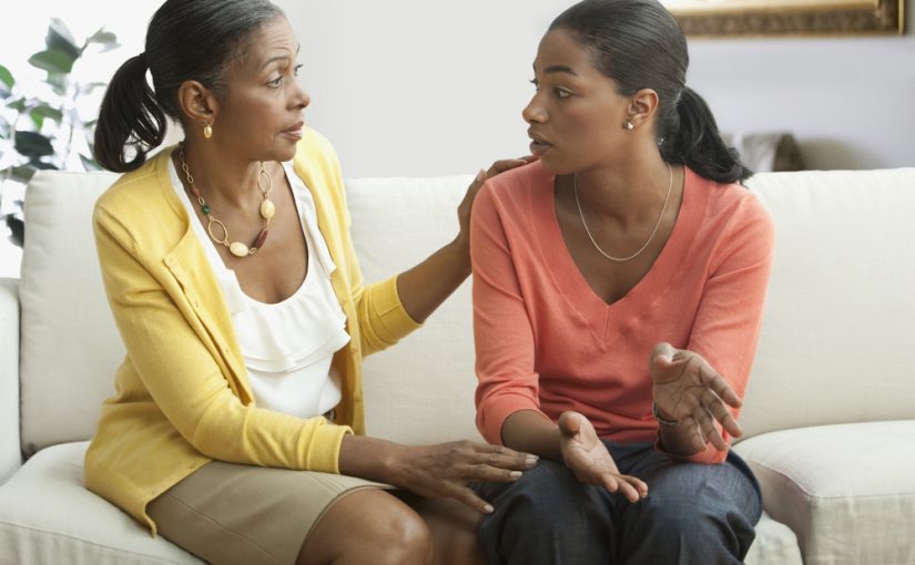 Two black women form different generations sitting on a couch, discussing a recovery aftercare program.